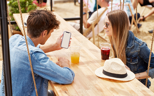 Young couple of freinds sitting drinking ice juice taliking and looking at blank screen of smartphone photo