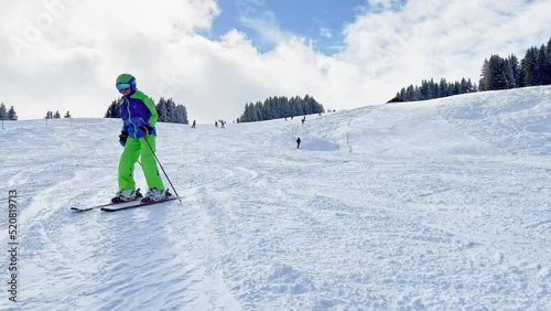 Child ski downhill to camera on skiing track at alpine resort