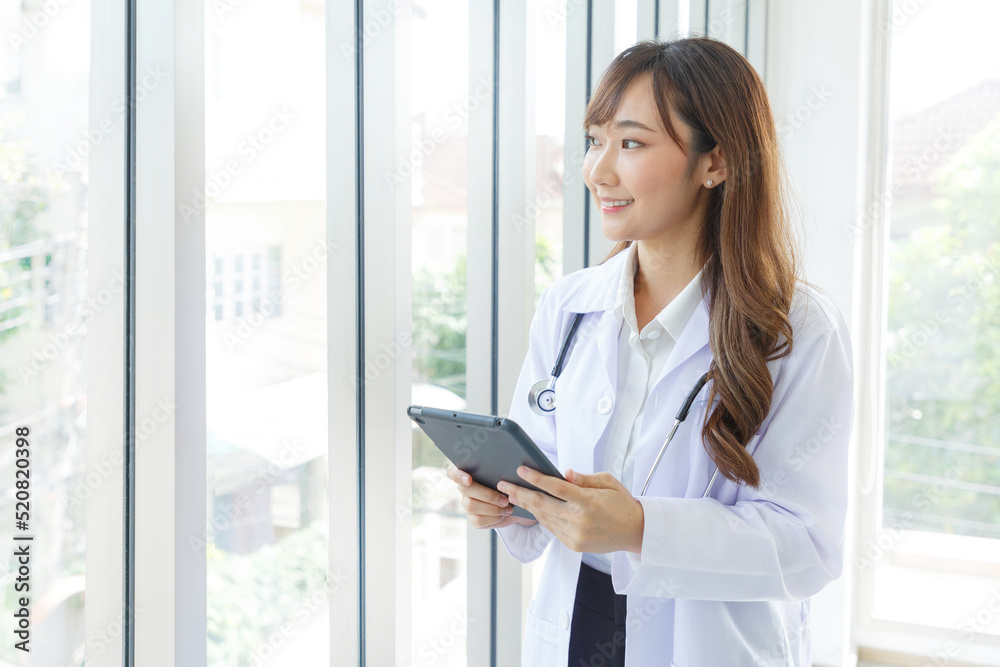 Beautiful and cheerful good mood young lady asian doctor dressed uniform smiling arm stethoscope while using tablet on lobby hospital background. Beautiful and cheerful good mood young lady asian doctor dressed uniform smiling arm stethoscope while using tablet on lobby hospital background.