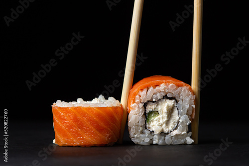 Chopsticks hold a roll on a black background. Traditional Japanese food.