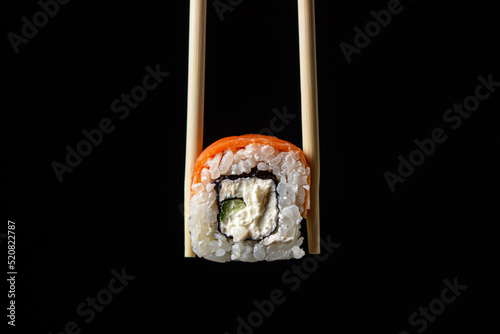 Chopsticks hold a roll on a black background. Traditional Japanese food.