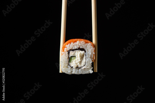 Chopsticks hold a roll on a black background. Traditional Japanese food.