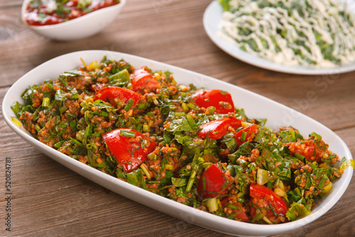 Tabbouleh salad with bulgur, tomatoes, parsley and green onion in plate on wooden table. Traditional middle eastern or arab dish. © vigenmnoyan