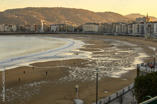 view of La Concha beach in San Sebastían half in darkness at low tide at half height the buildings of the city, in the background Mount Ulia on which the first almost horizontal rays of dawn can be se photo