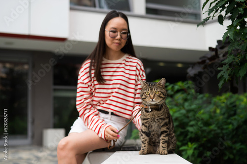 Obraz na plátně Young woman and tabby cat sitting on a bench outdoors.