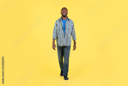 African Guy Walking Smiling Looking At Camera Over Yellow Background