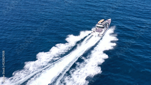 Aerial drone photo of small speed boat with dual outboards cruising in high speed deep blue Aegean sea