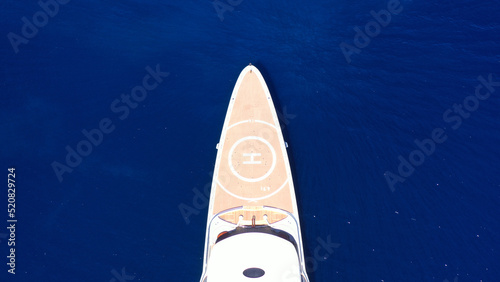 Aerial drone top down photo of luxury mega yacht with wooden deck and helipad anchored in deep blue Mediterranean sea