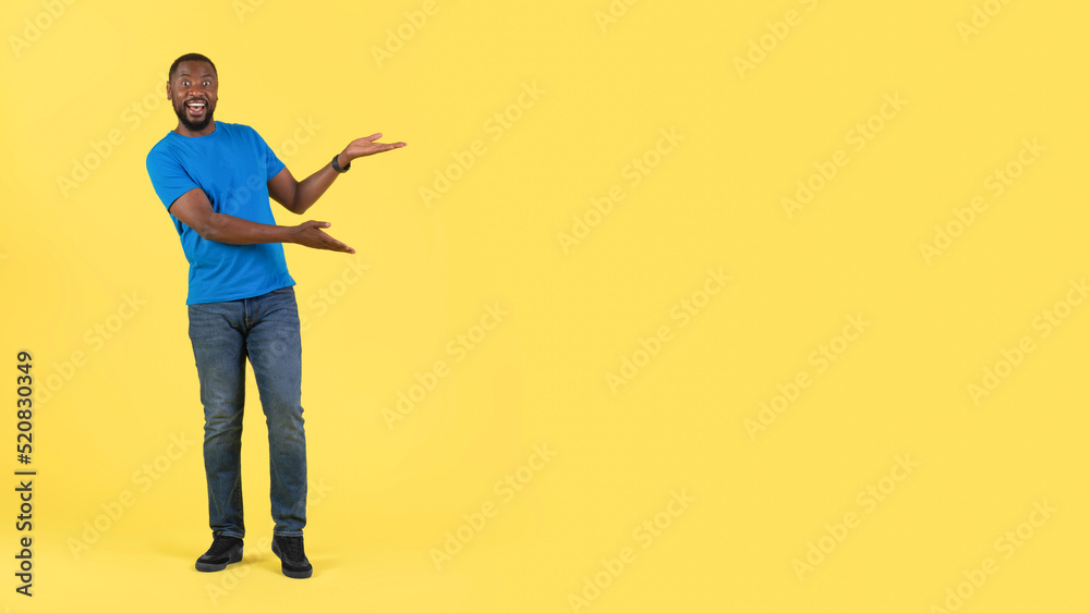 Fototapeta premium Excited Black Guy Gesturing Pointing At Free Space, Yellow Background