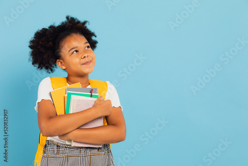 Happy African American schoolgirl holding books on blue background, back to school concept. photo