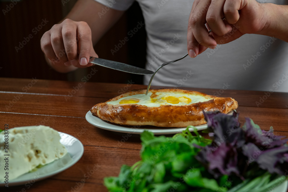 Man eating adjar Khachapuri. Georgian national pie khachapuri with egg and cheese in the white plate  on wooden background.