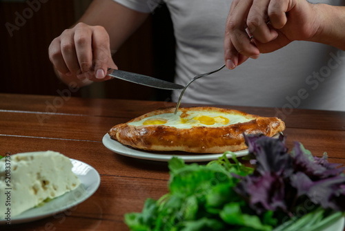 Man eating adjar Khachapuri. Georgian national pie khachapuri with egg and cheese in the white plate on wooden background.