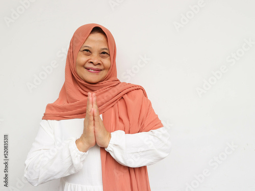 Beautiful face of happy mature middle-aged woman in hijab. Elderly woman in turban, healthy cheerful smiling, looking at camera with hand gesture greeting "Happy Eid Al-Fitr"