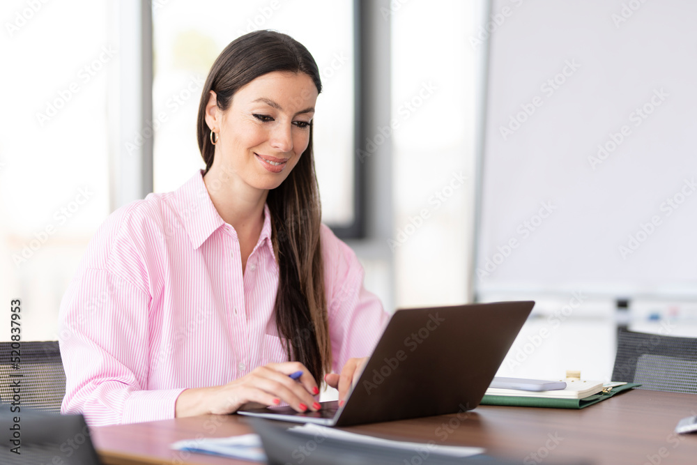 Confident businesswoman using a laptop while sitting at the office Confident businesswoman using a laptop while sitting at the office