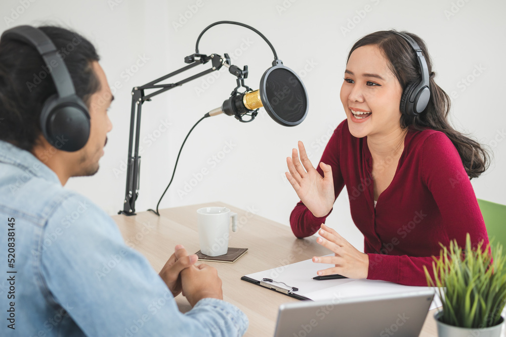 Naklejka premium Smile two asian young woman, man radio hosts in headphones, microphone while talk, conversation, recording podcast in broadcasting at studio together. Technology of making record audio concept.