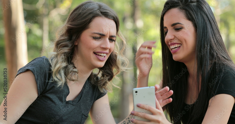 Authentic friends together outdoors checking cellphone Girls looking and holding smartphone chatting exchanging gossip