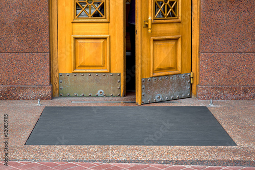 stone threshold with black rubber foot mat at opening yellow door made of wood and granite stone facade cladding of retro European architecture building close up front view, nobody. photo