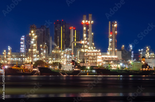 Oil refinery plant from industry zone, Aerial view oil and gas petrochemical industrial, Refinery factory oil storage tank and pipeline steel Oil tankers are loading oil to the ship. at night