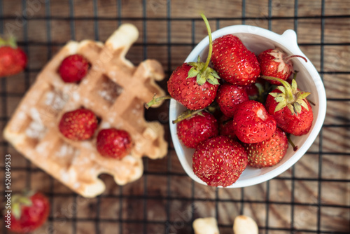 Fresh strawberries in a bowl and with viennese waffles on a wooden table top view