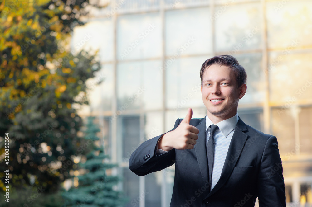Great job! Happy young business man in formal wear showing his thumb up while standing against building structure Great job! Happy young business man in formal wear showing his thumb up while standing against building structure