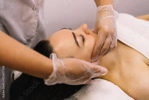 Woman receiving facial buccal massage in beauty salon.Beauty and skincare concept with a beautiful woman. Middle aged female relaxed with massage for facial lifting photo