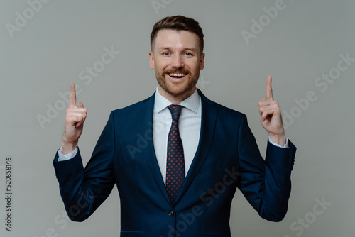 Happy businessman in suit pointing up with fingers and smiling at camera photo