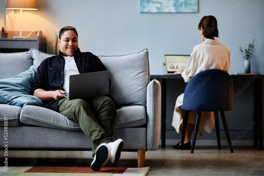 Portrait of modern multiethnic woman relaxing on couch at home and using laptop, copy space Portrait of modern multiethnic woman relaxing on couch at home and using laptop, copy space