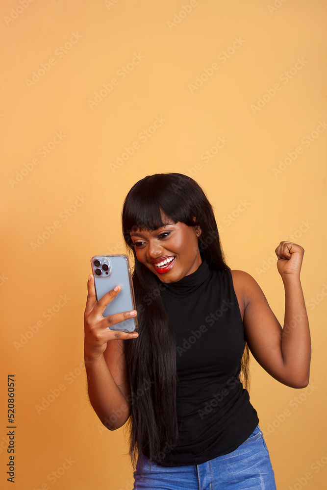 Excited young woman watching her phone in the street. Winning girl celebrating with mobile in her hand on isolated background Excited young woman watching her phone in the street. Winning girl celebrating with mobile in her hand on isolated background