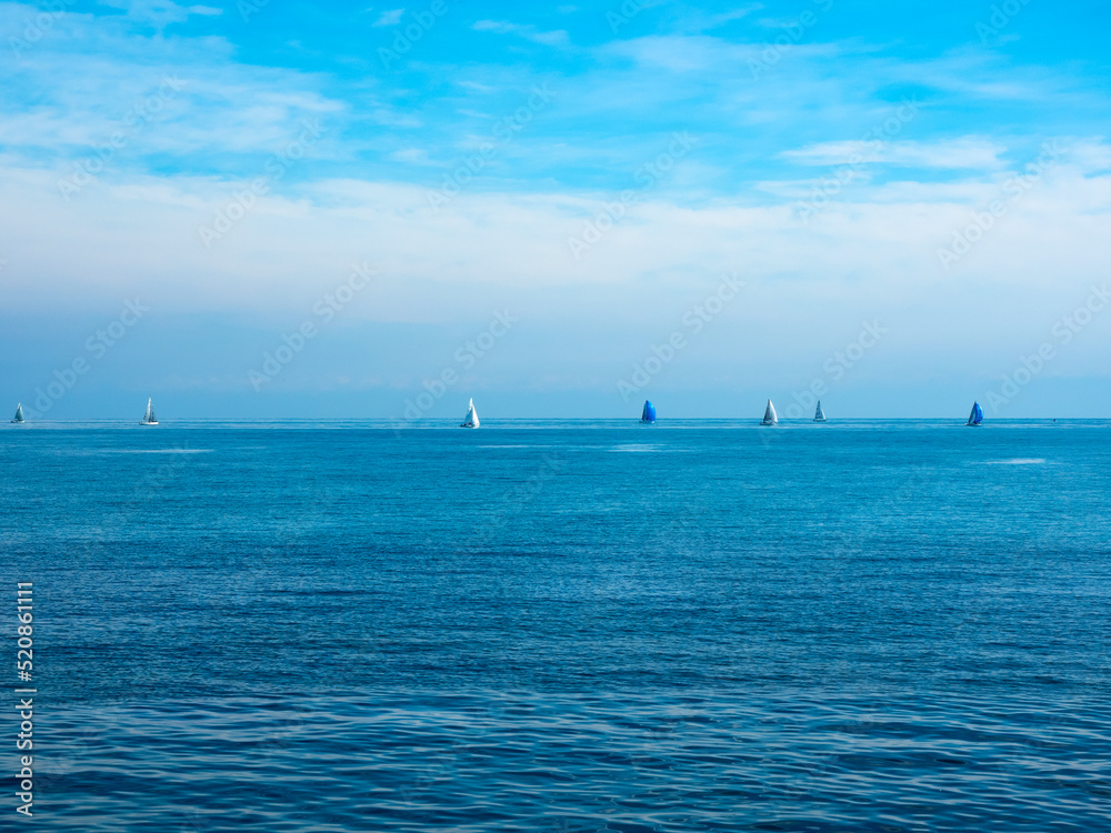 the bright sun in the morning illuminates the sea and sky of an intense blue. on the horizon white sails and blue sails