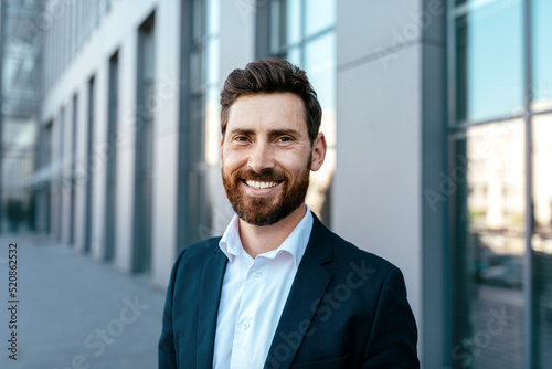 Portrait of smiling confident attractive millennial businessman with beard in suit looking at camera photo