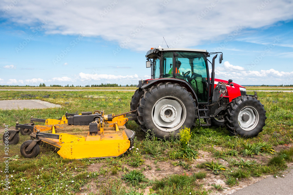 Wheeled tractor with rotary mower in the field next to the road Wheeled tractor with rotary mower in the field next to the road