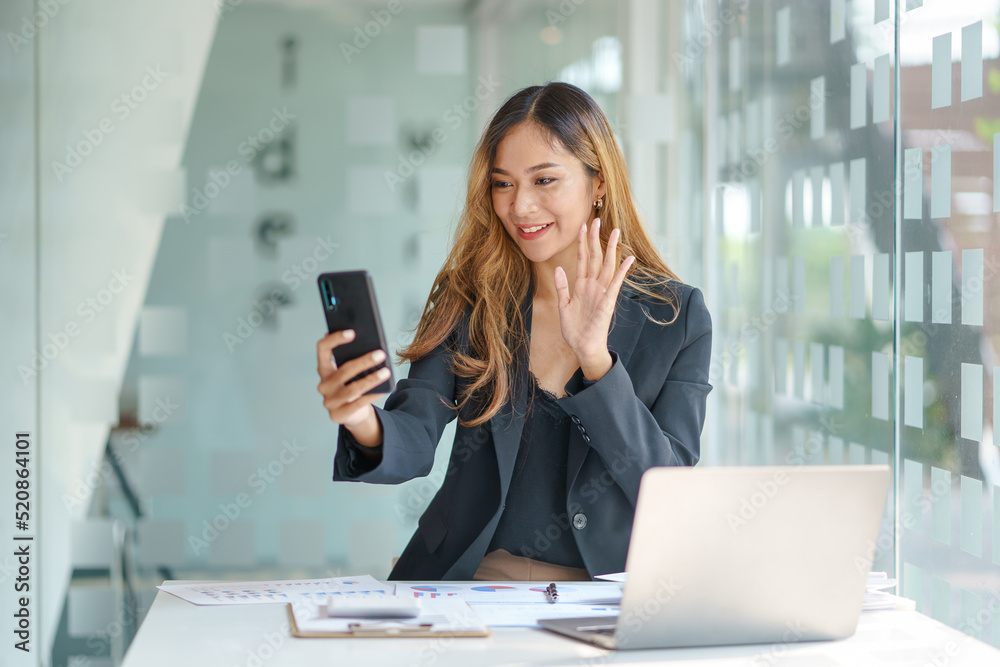 Beautiful Asian businesswoman having fun on the phone for a video call with a customer in the office. Beautiful Asian businesswoman having fun on the phone for a video call with a customer in the office.