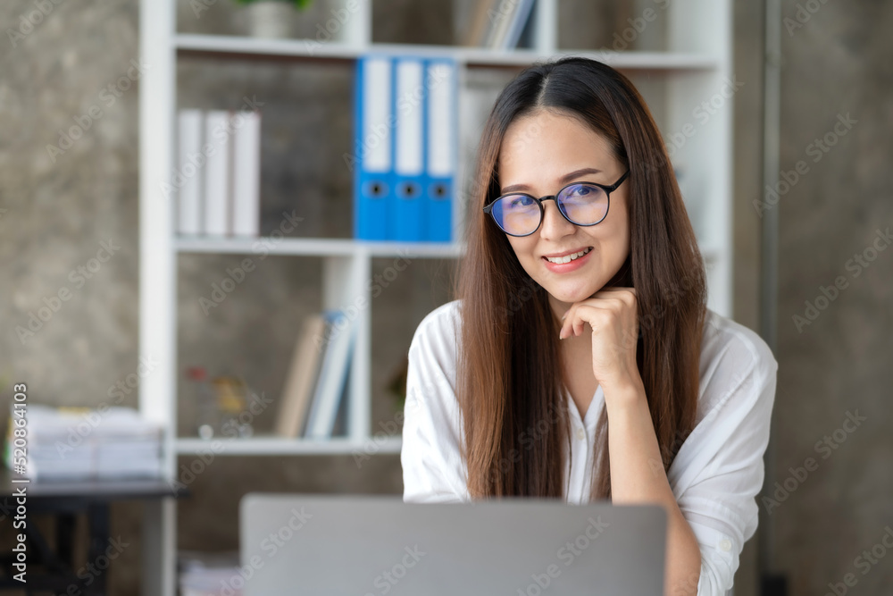 Beautiful Asian businesswoman sitting and smiling at the camera at work happily in the office. Beautiful Asian businesswoman sitting and smiling at the camera at work happily in the office.
