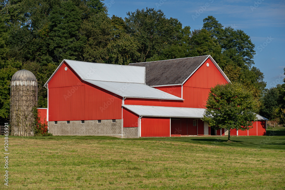 Red barn with a short silo with large green trees in the background