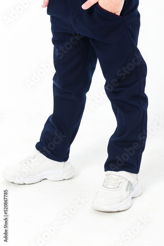Little boy posing in school uniform - in trousers and white sneakers on a white background.