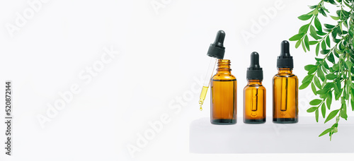 Natural medicine or aroma oil or beauty essence concept mockup three vials with dropper with droplet on glass stand with green plant and white background. Face and body spa serum care concept banner