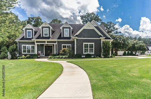 A large gray craftsman new construction house with a landscaped yard and leading pathway sidewalk