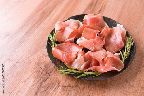 Charcuterie plate with proscuitto served with olives at wooden table background with copy space. Black plate with traditional italian antipasti. Selective focus photo