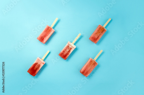 Fruit icecream on wooden stick and blue background. Minimal hot summer concept. Selective focus