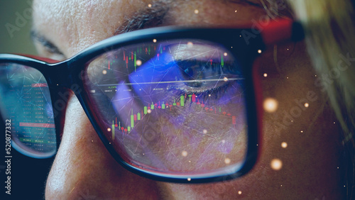Macro shot of a woman working on a computer. Concept of technology, business and the stock market. Stock market graph reflection on the glasses. Selective focus.             