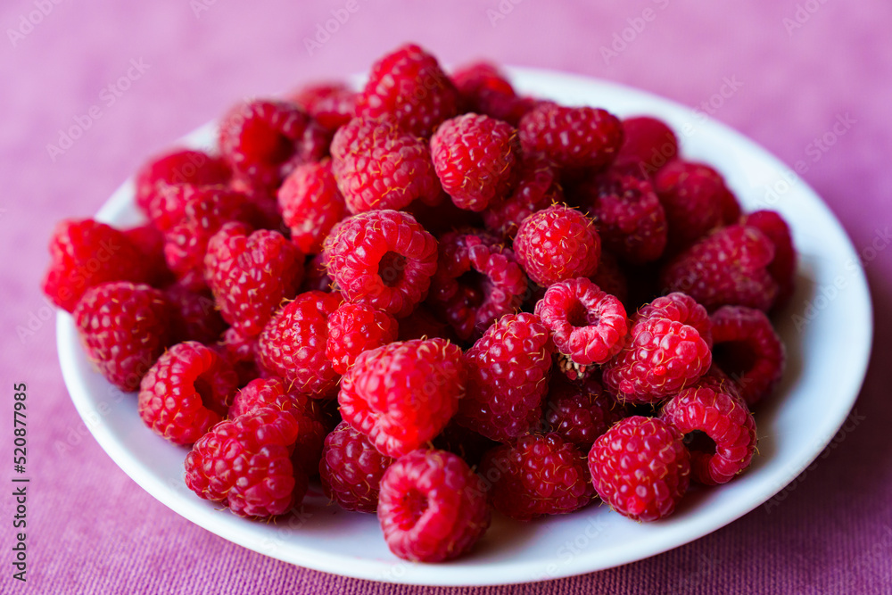a white plate with raspberries on the table. a white plate with raspberries on the table.