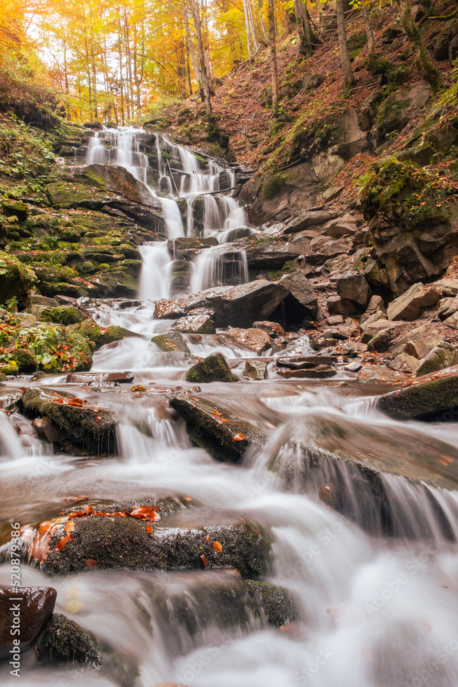 Fototapeta premium Beautiful waterfall with trees, red leaves, rocks and stones in autumn forest