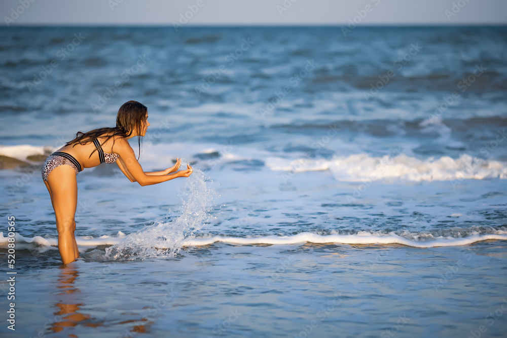 A girl with loose hair walks on the sea with waves and enjoys the sun