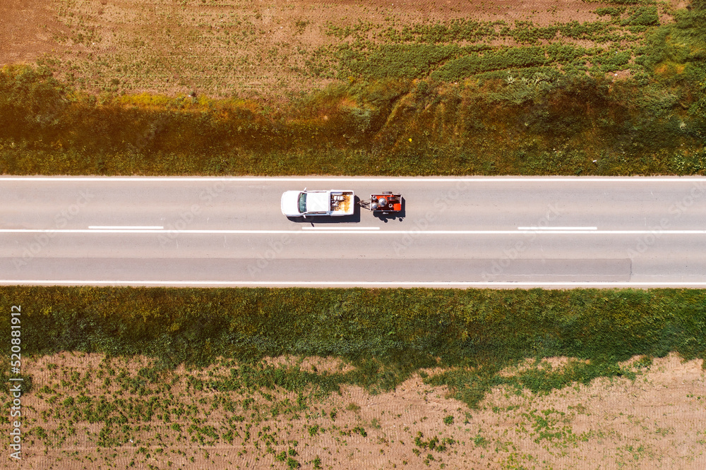 Aerial shot of pickup truck with trailer on highway through countryside landscape, drone pov - obrazy, fototapety, plakaty 