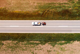 Aerial shot of pickup truck with trailer on highway through countryside landscape, drone pov