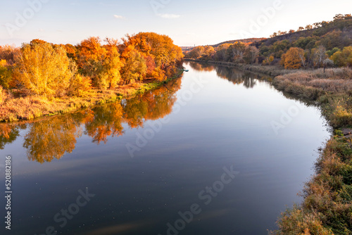 Multicolored autumn trees in the sun on the river bank. Autumn landscape. Bright colors of autumn by the river.