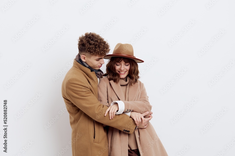 a cute couple is standing on a light background dressed in coats and sweaters, a man and a woman are looking down confusedly hugging each other a cute couple is standing on a light background dressed in coats and sweaters, a man and a woman are looking down confusedly hugging each other