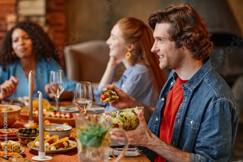 Side view portrait of young man talking to friends at table during dinner party in cozy setting  copy space