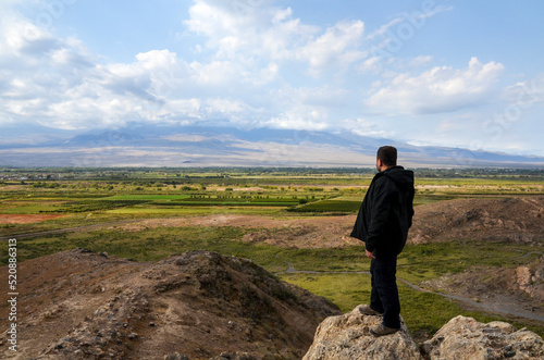 Rear view of a man standing, looking and enjoying of a scenic landscape a valley with mount Ararat hidden by clouds