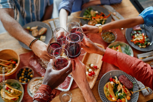 Top down view of young people toasting with wine glasses while celebrating at dinner party together, copy space